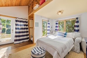 Ein Schlafzimmer mit einem Bett, einem Fenster, Vorhängen und einer Holzbalkendecke.