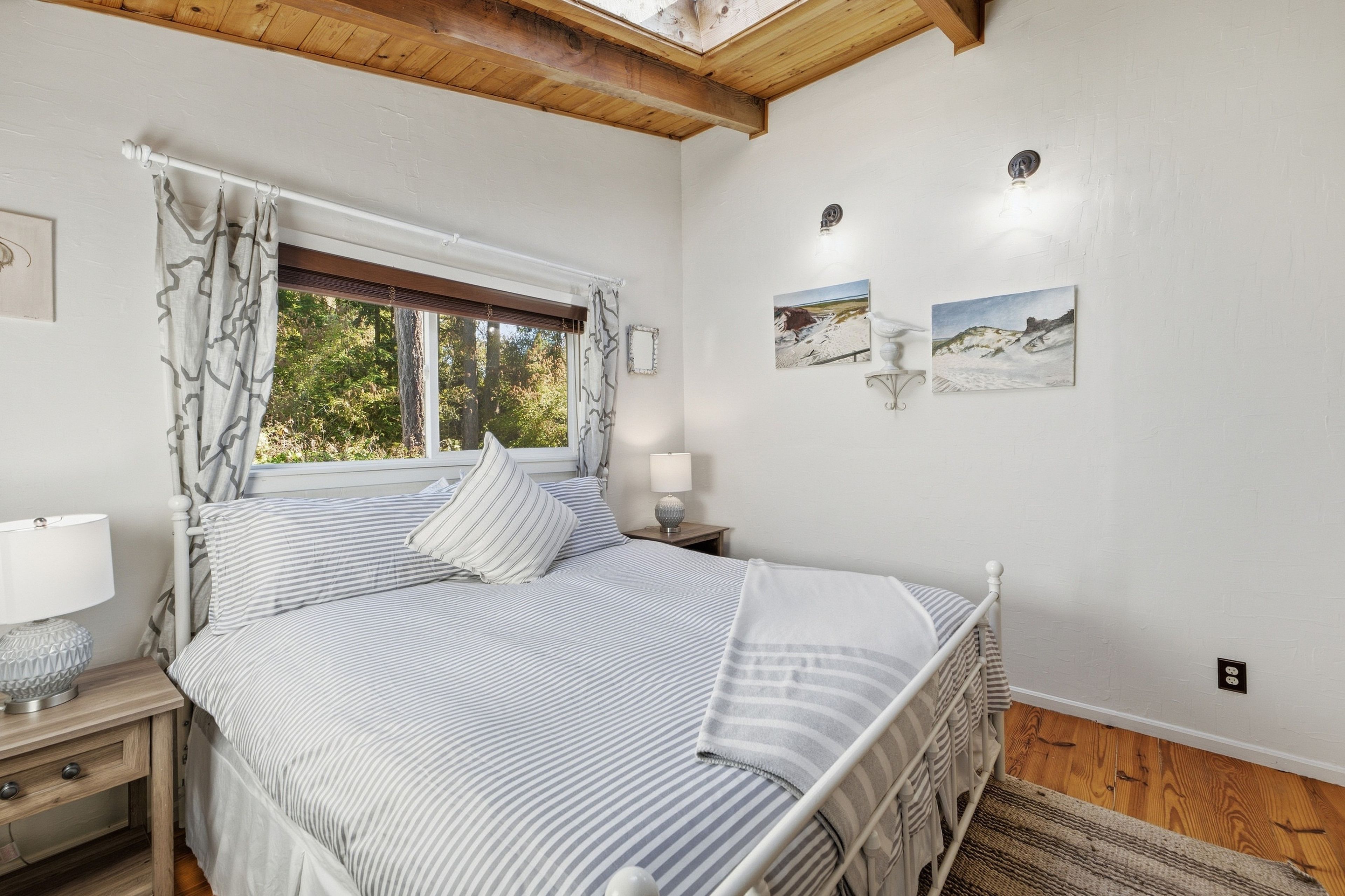 A bedroom with a bed, a window with curtains, a bedside lamp, and two wall-mounted picture frames.