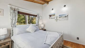 A bedroom with a bed, a window with curtains, a bedside lamp, and two wall-mounted picture frames.