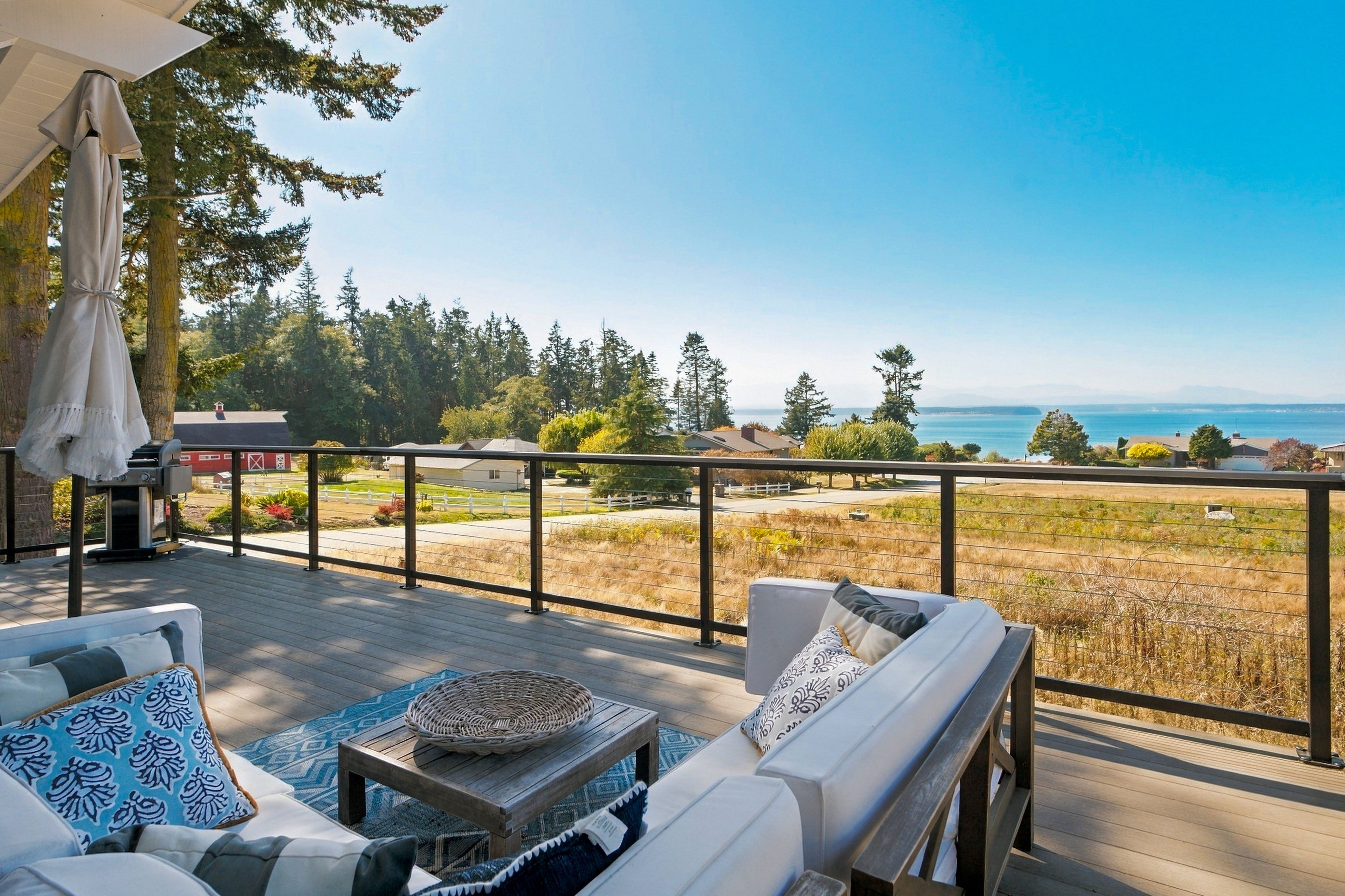 A deck with outdoor furniture, a view of the ocean, and a forested landscape.