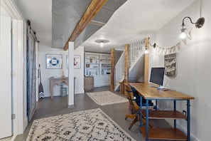 A spacious living area with a wooden dining table, a computer desk, and a staircase leading to an upper level.