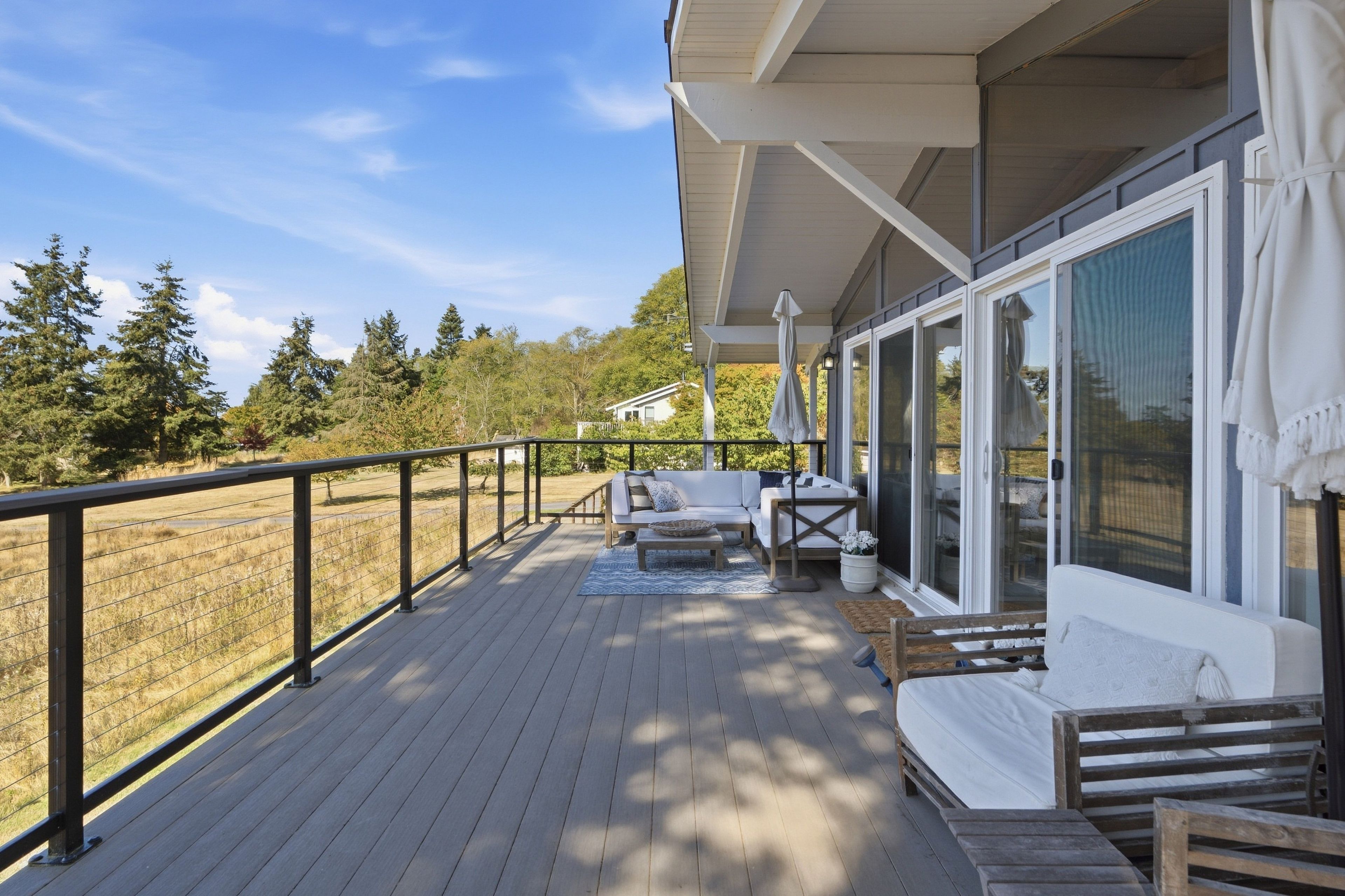A deck with a sofa and a table, overlooking a grassy area with trees.