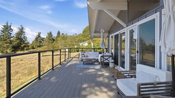 A deck with a sofa and a table, overlooking a grassy area with trees.