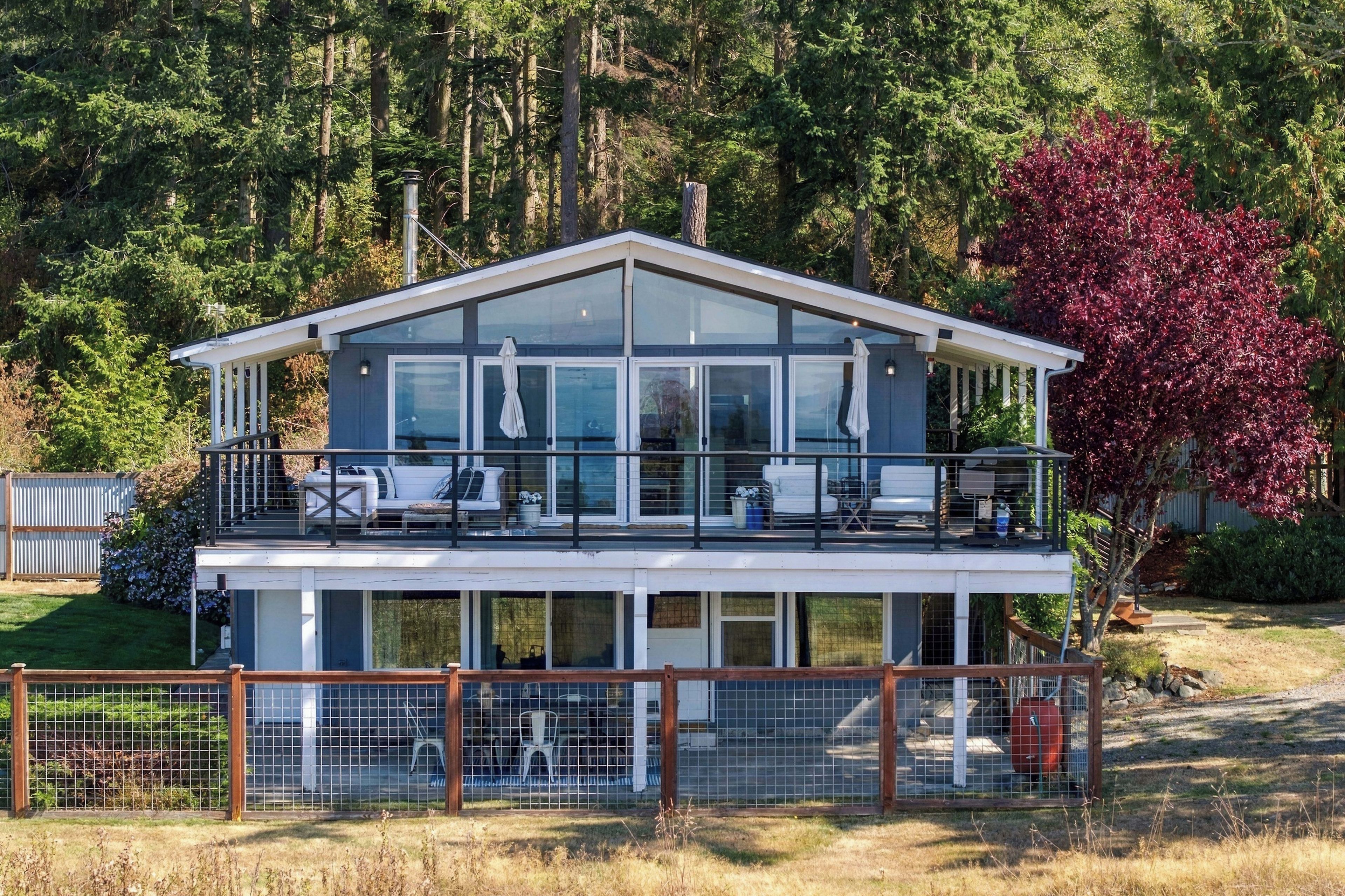 A two-story modern house with a balcony, large windows, and a fenced yard.