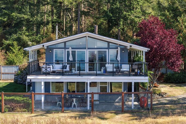 A two-story modern house with a balcony, large windows, and a fenced yard.