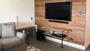 Una sala de estar con una televisión de pantalla plana montada en una pared de madera, un sofá gris y una pequeña mesita con una vela.