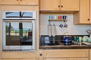 A kitchen with a built-in oven, a spice rack, and a coffee station.