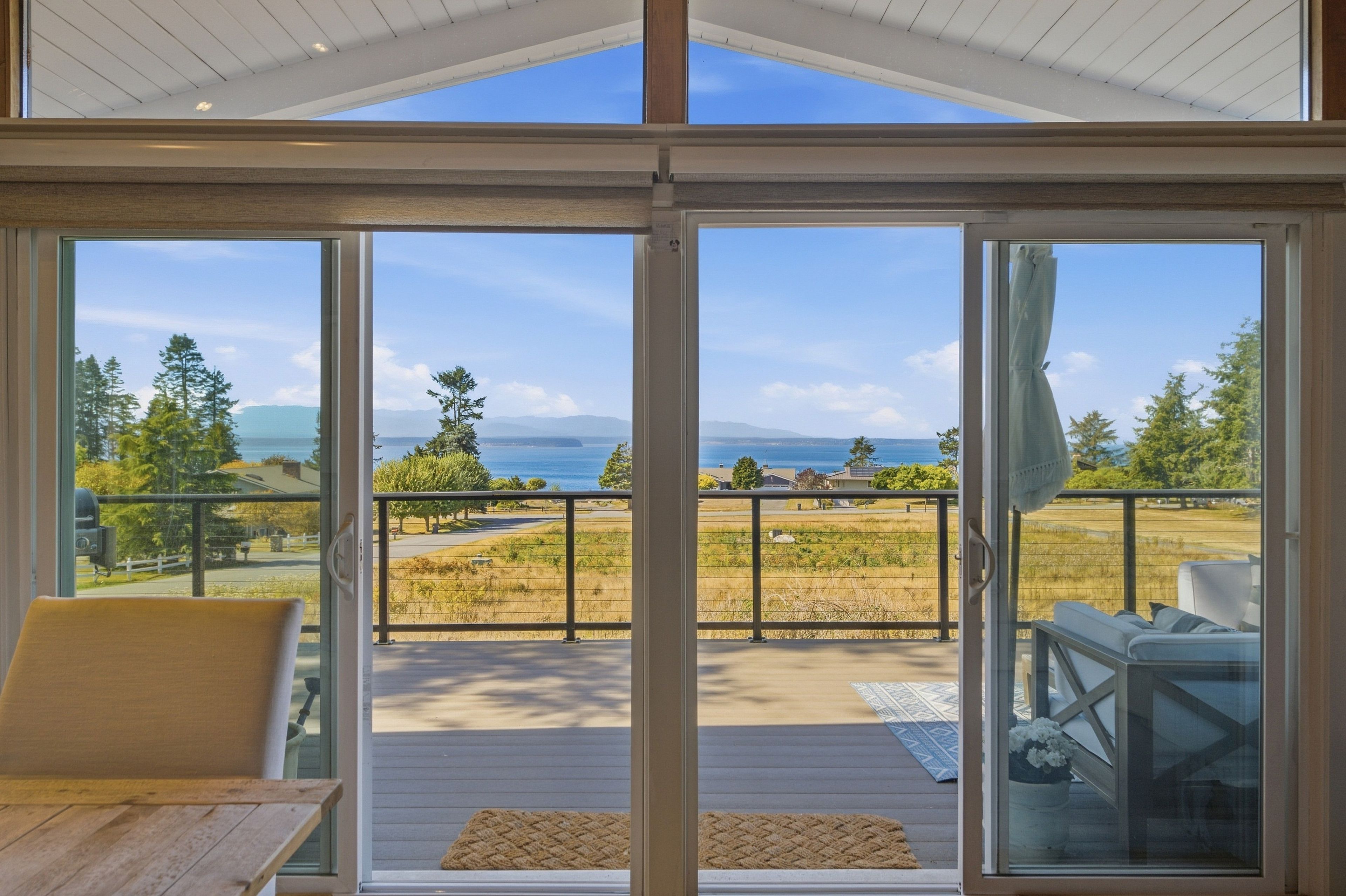 A room with a large sliding glass door leading to an outdoor deck with a view of a body of water and mountains.