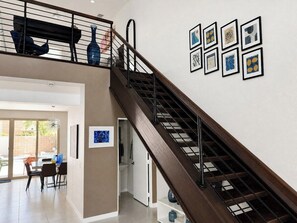 A modern interior with a wooden staircase, a dining area with chairs, and a wall with framed artwork. - Oceo Oasis - South Palm Springs (Palm Springs)