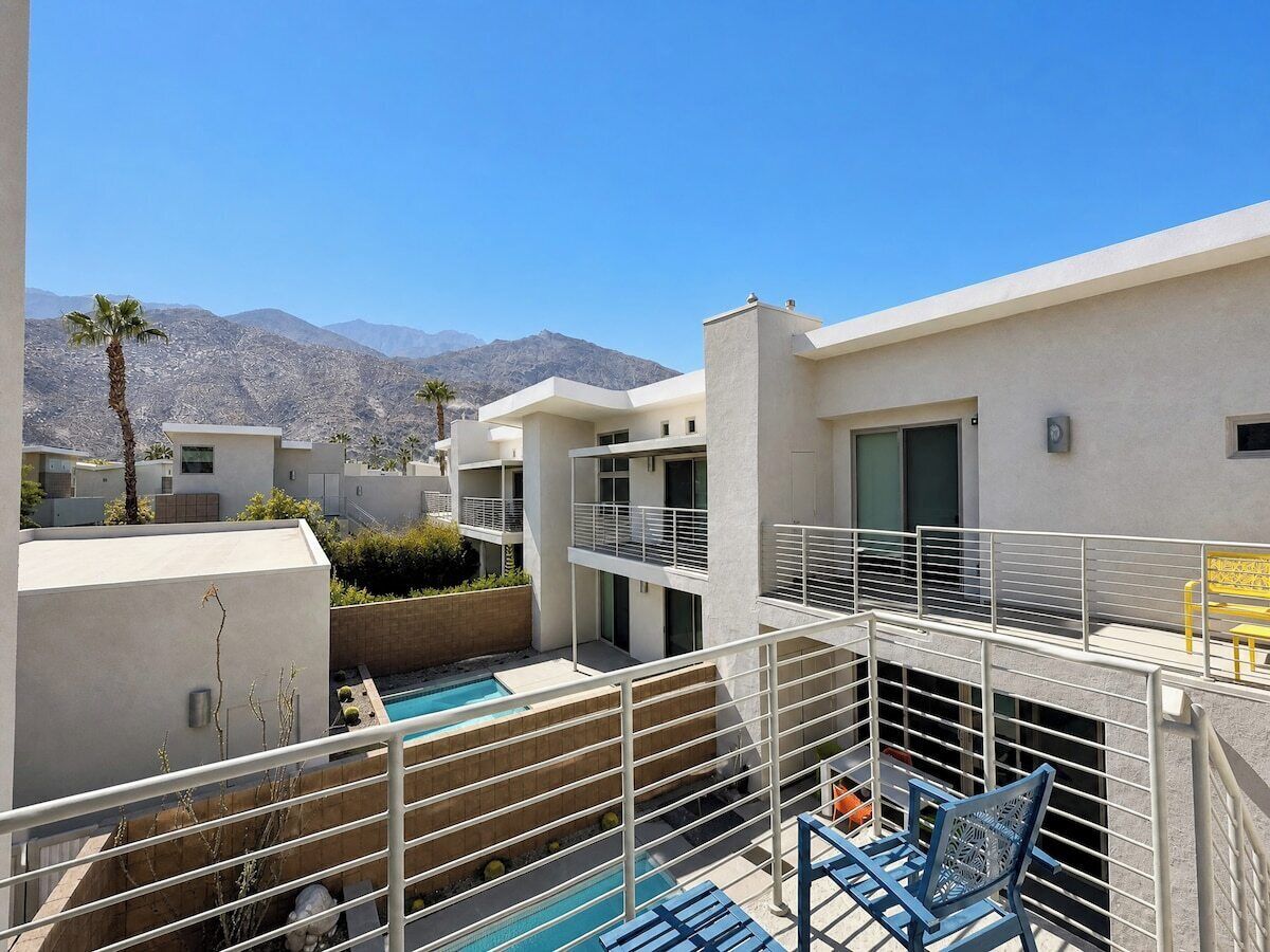 A modern residential building with a pool, balconies, and a mountain view.