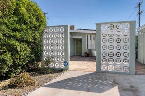 Una entrada con reja y celosía blanca decorativa, un camino empedrado y una puerta verde.