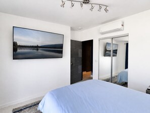 Ein Schlafzimmer mit einem Bett, einem großen Fenster, einer Tür und einer Wand-Klimaanlage.