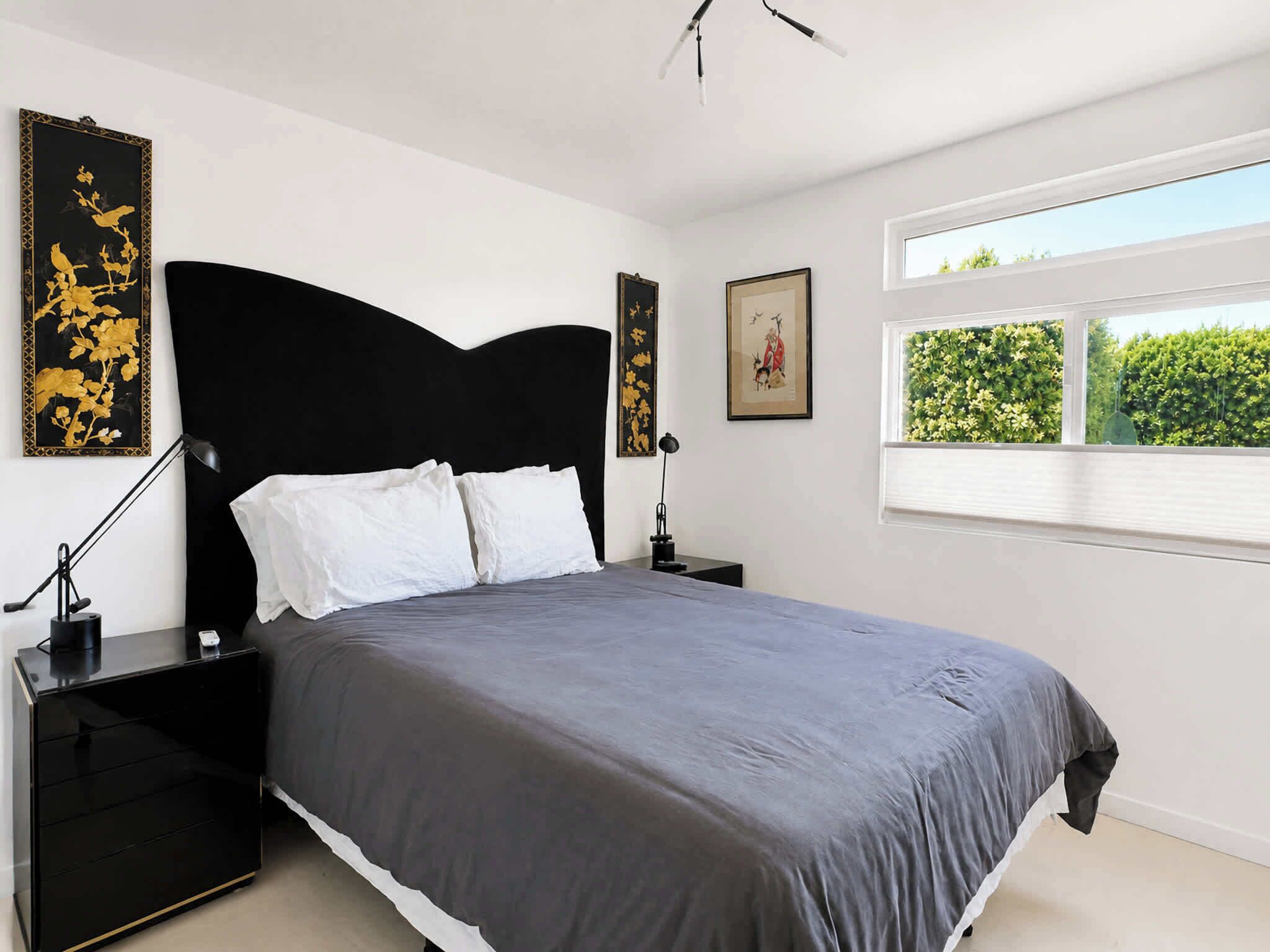 Une chambre à coucher moderne avec un grand lit, une table de chevet, une lampe et des œuvres d’art accrochées aux murs.