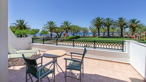 Eine Terrasse mit Sitzgelegenheit, Meerblick und Palmen.