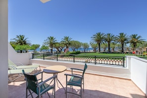 Una terraza con asientos al aire libre, vista al mar y palmeras.