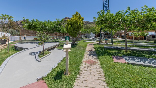 Ein gepflasterter Weg mit einem grünen Wegweiser, umgeben von Gras und Bäumen, der zu einem Gebäude mit geneigtem Dach führt.