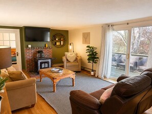 Ein Wohnzimmer mit Kamin, einer Couch, einem Couchtisch und einem großen Fenster mit Blick auf Gartenmöbel.