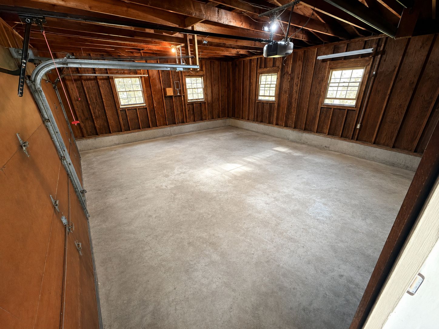 A spacious, unfinished room with concrete flooring, wooden walls, and a slanted ceiling.