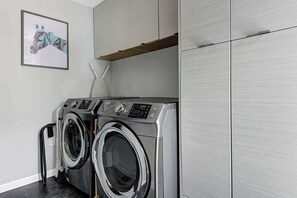 A laundry area with two front-loading washing machines, a towel rack, and a framed picture on the wall. - Stylish Palm Springs Retreat | Pool & Spa (Palm Springs)