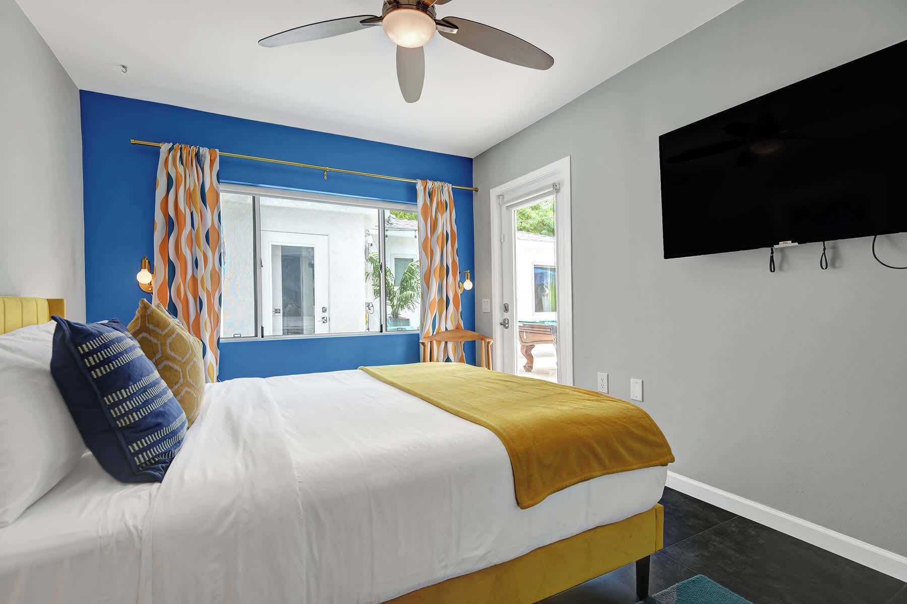 A bedroom with a bed, a ceiling fan, a TV, and a window with curtains.