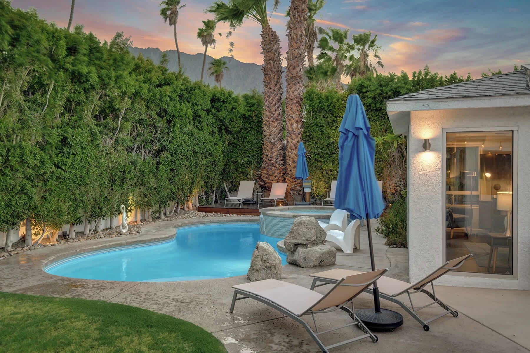 A swimming pool with lounge chairs and umbrellas, surrounded by greenery and a mountain backdrop.