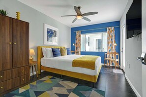 A bedroom with a bed, a ceiling fan, a window with curtains, a bedside table with a lamp, and a wall-mounted TV. - Stylish Palm Springs Retreat | Pool & Spa (Palm Springs)