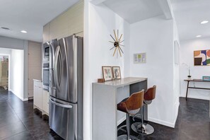 A modern kitchen with a stainless steel refrigerator, a built-in oven, and a bar area with two stools. - Stylish Palm Springs Retreat | Pool & Spa (Palm Springs)