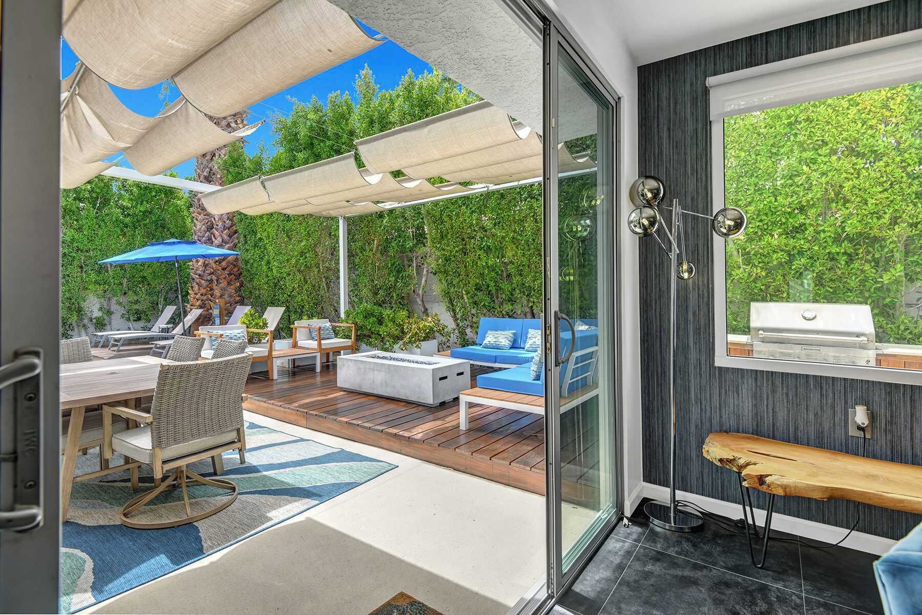 A modern outdoor patio with a wooden deck, lounge chairs, and a barbecue grill.