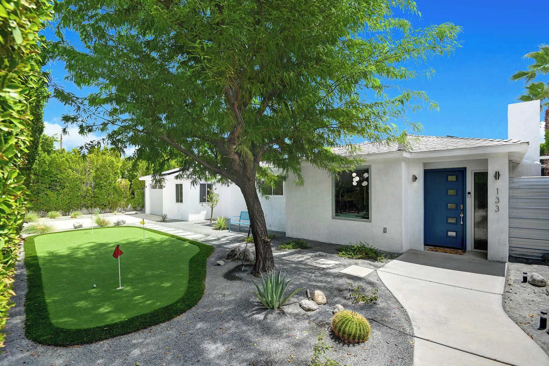 A residential property with a well-maintained lawn, a blue door, and a small garden with cacti and rocks.