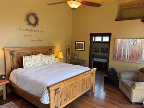 A bedroom with a wooden bed, a nightstand, a bedside lamp, a framed picture, a wall-mounted artwork, and a view into a bathroom. - 3-bedroom, 2-bath gated community of Blue River Valley Ranch Lakes (Silverthorne)