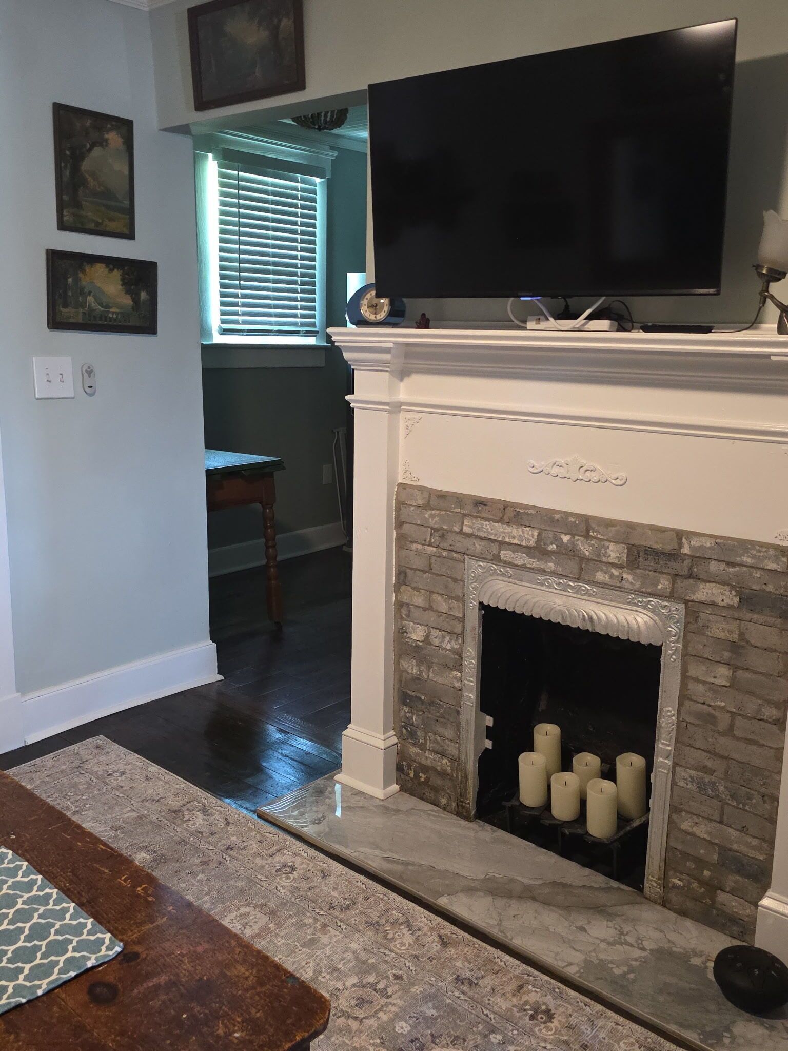 A living room with a fireplace, a television mounted above it, and a dining area visible through a window.