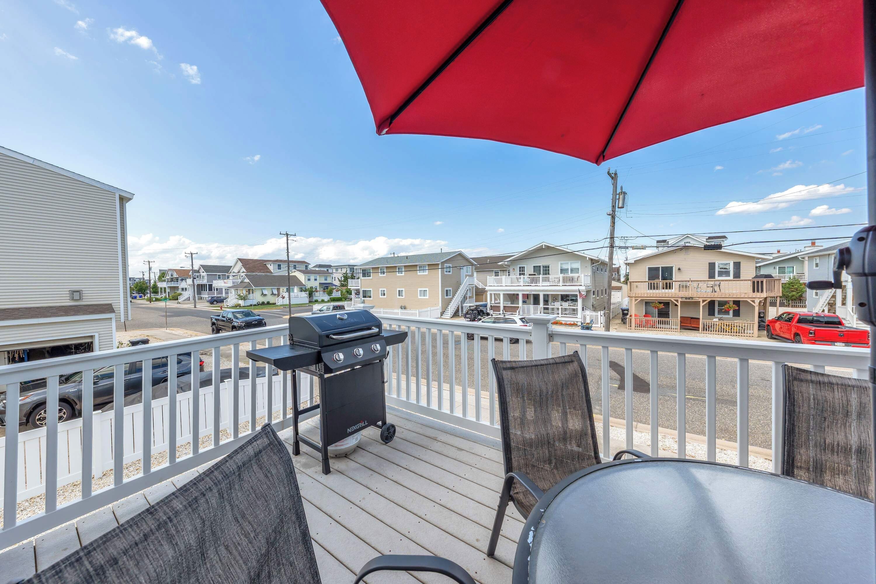 A deck with a grill, chairs, and a red umbrella.