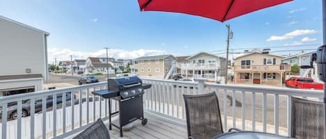 A deck with a grill, chairs, and a red umbrella.
