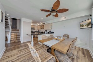 A modern kitchen with white cabinets, a central island, and a dining area with a wooden table and wicker chairs. - Rooftop Deck & Sunset Views, Avalon House (Avalon)