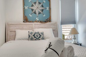A neatly made bed with a decorative pillow, a wall-mounted compass, and a lamp on a bedside table. - Rooftop Deck & Sunset Views, Avalon House (Avalon)