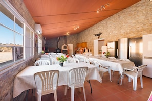 A restaurant with multiple tables and chairs, a stone wall, and a view of the desert through large windows. - Apartment 'Quarto 4' with Wi-Fi and Air Conditioning (Corte do Pinto)