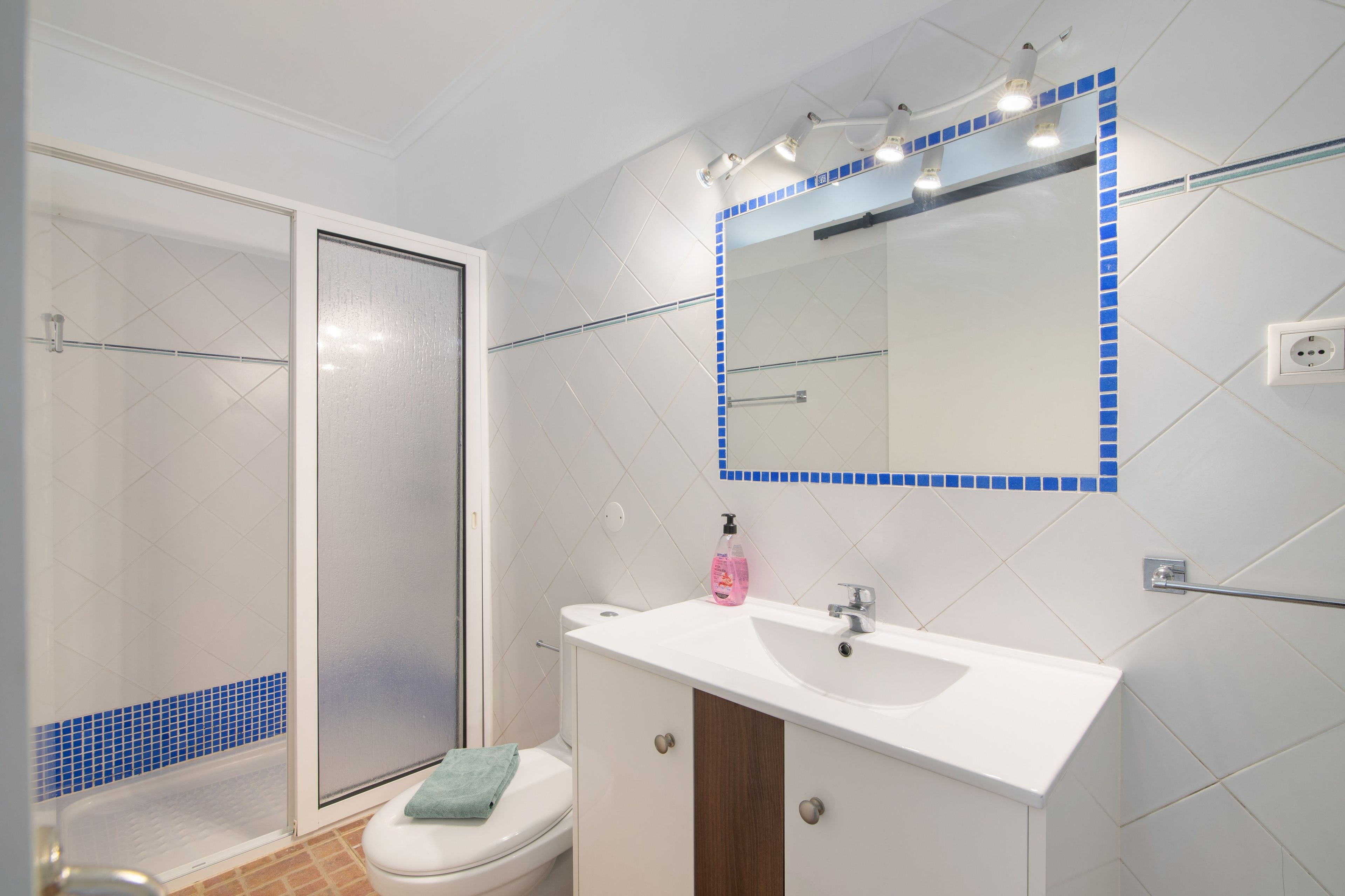Een badkamer met een wit wastafelmeubel, een spiegel met blauwe lijst en een douche.
