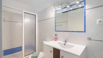 Een badkamer met een wit wastafelmeubel, een spiegel met blauwe lijst en een douche.