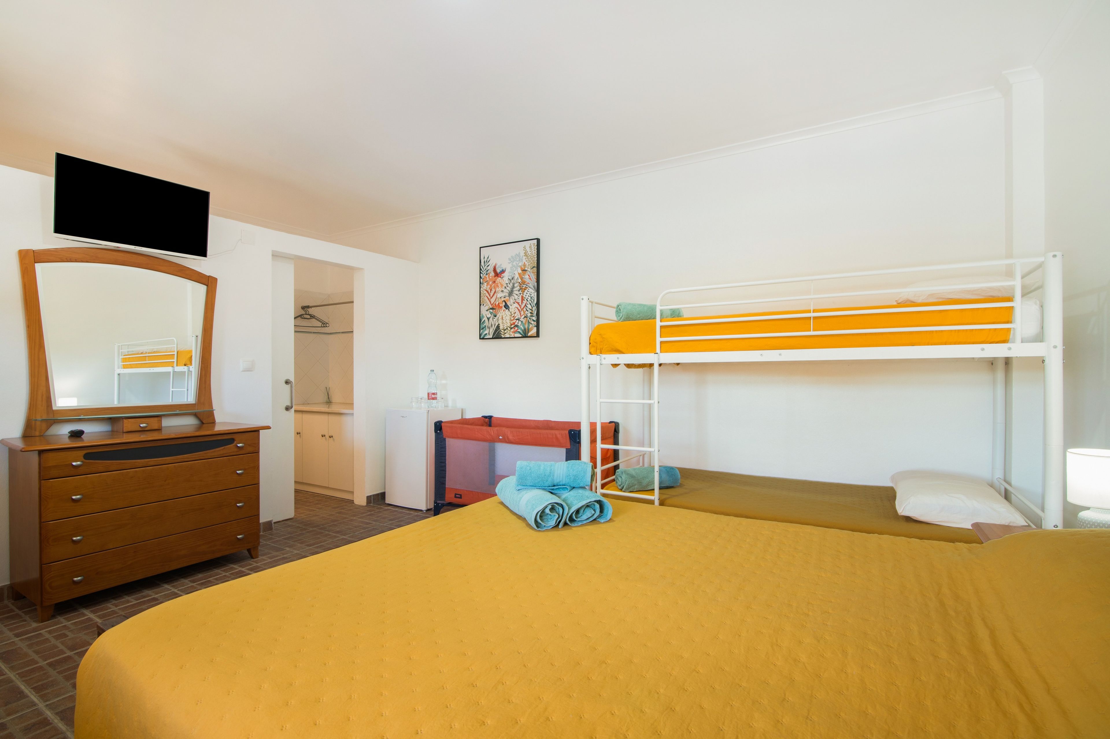 Ein Hotelzimmer mit Etagenbett, Kommode, Spiegel, Fernseher und einer kleinen Küche.