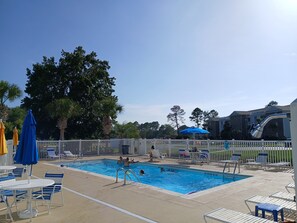 A swimming pool with lounge chairs and umbrellas, surrounded by a white fence and trees. - Sunset Beach Sea Trail Champions suite!  New and nice! Great 1st floor location (Sunset Beach)