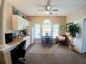A kitchen with white cabinets, a dining area with a table and chairs, a ceiling fan, and a large window. - Sunset Beach Sea Trail Champions suite!  New and nice! Great 1st floor location (Sunset Beach)
