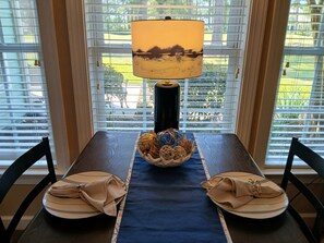 A dining table with a lamp, a bowl of decorative items, and two plates with folded napkins. - Sunset Beach Sea Trail Champions suite!  New and nice! Great 1st floor location (Sunset Beach)