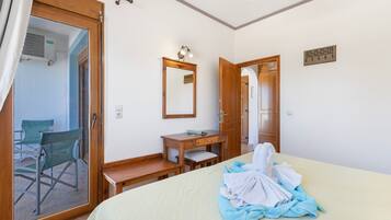 A hotel room with a bed, a desk, a chair, a mirror, and a door leading to another room.