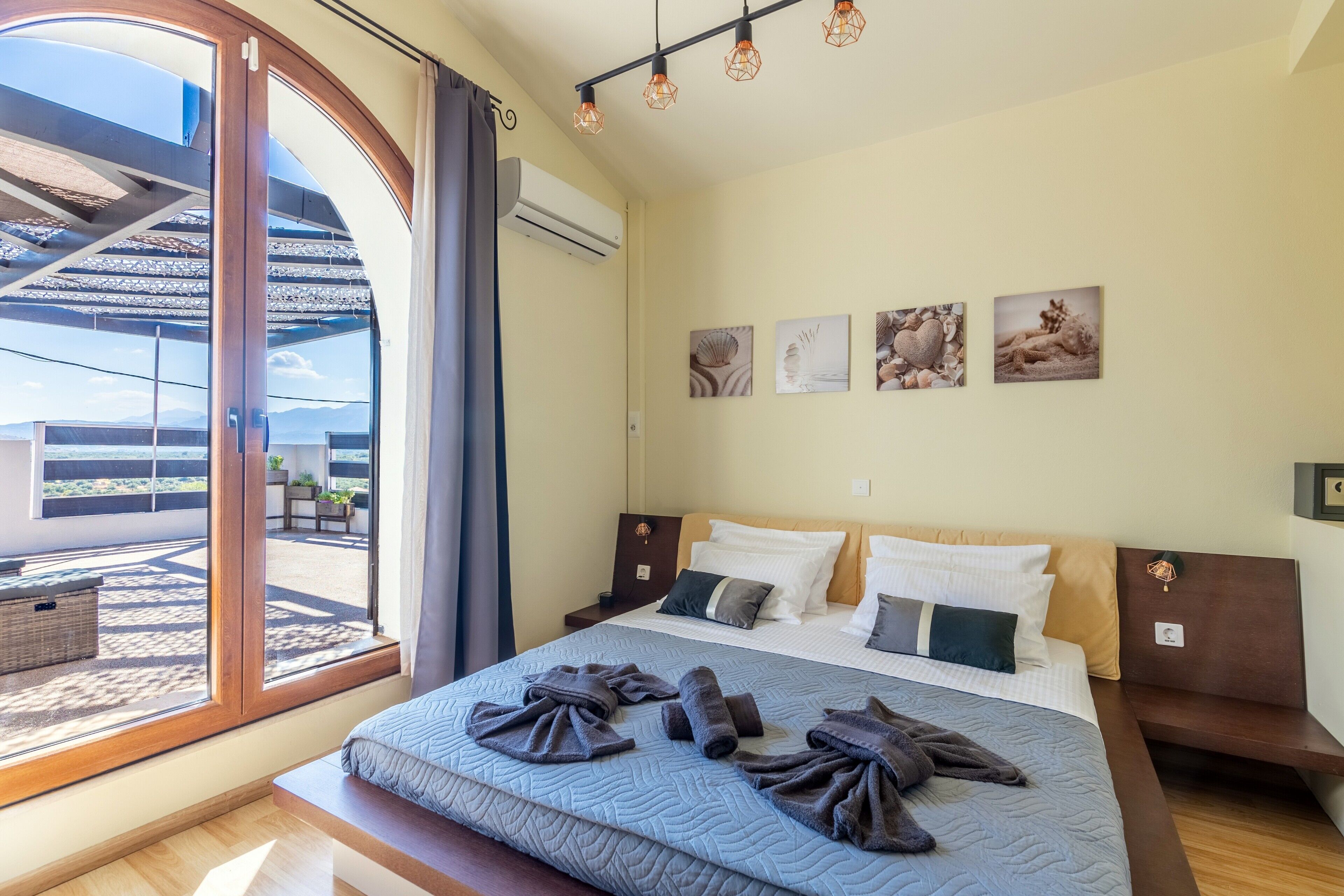 A hotel room with a large bed, a balcony with a view, and three wall-mounted artworks.