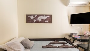Ein Hotelzimmer mit einem Bett, Kissen, einer Weltkarte als Wandbild, einem Fernseher und einem Schreibtisch mit Ventilator und Büchern.