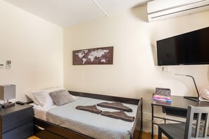 A hotel room with a bed, a desk, a chair, a television, and a world map artwork on the wall.