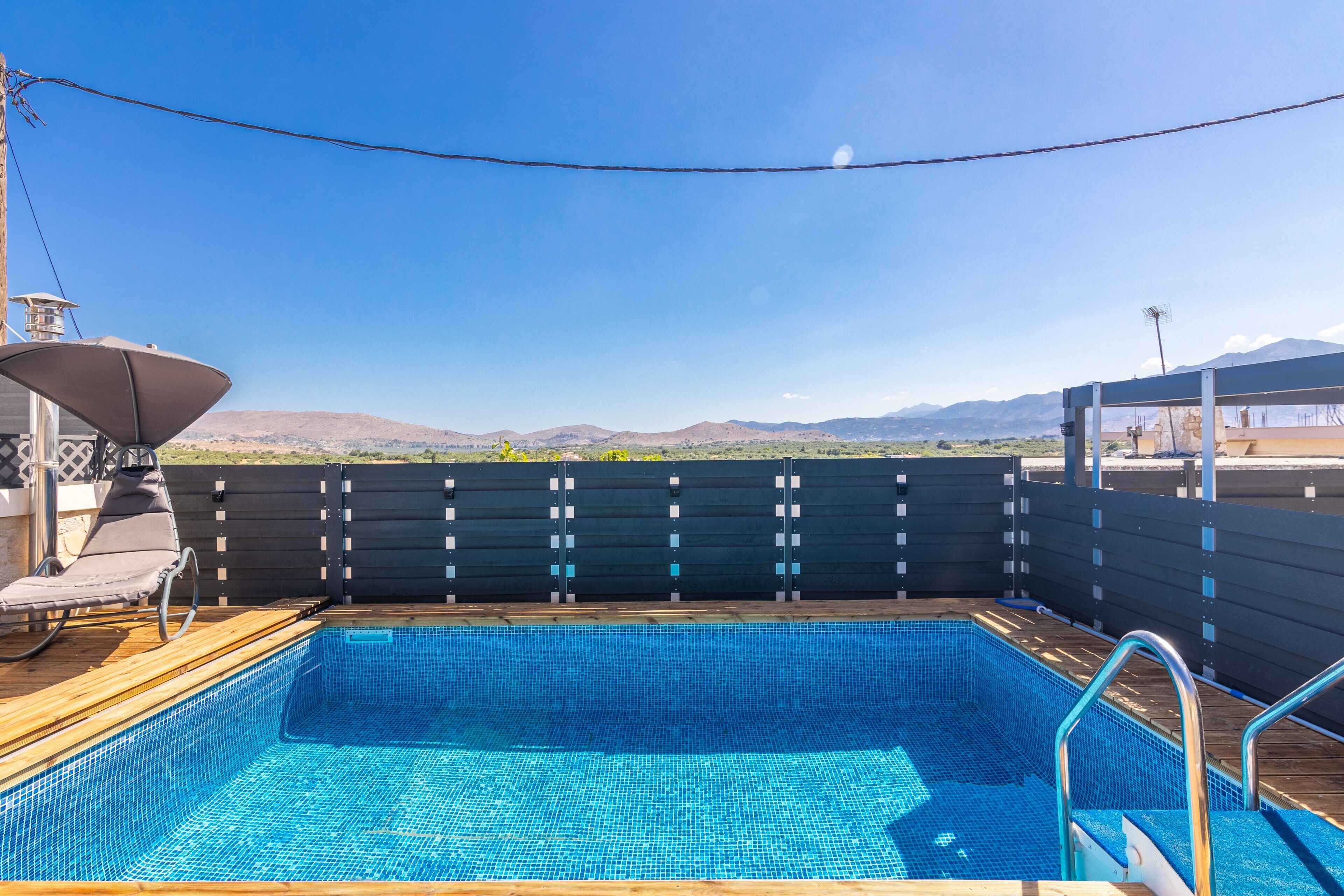 A pool area with a view of mountains, a lounge chair, and a wooden deck.
