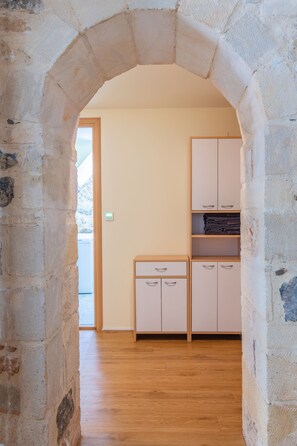 A room with a stone archway leading to a wooden floor, a white cabinet with drawers, and a built-in shelving unit.