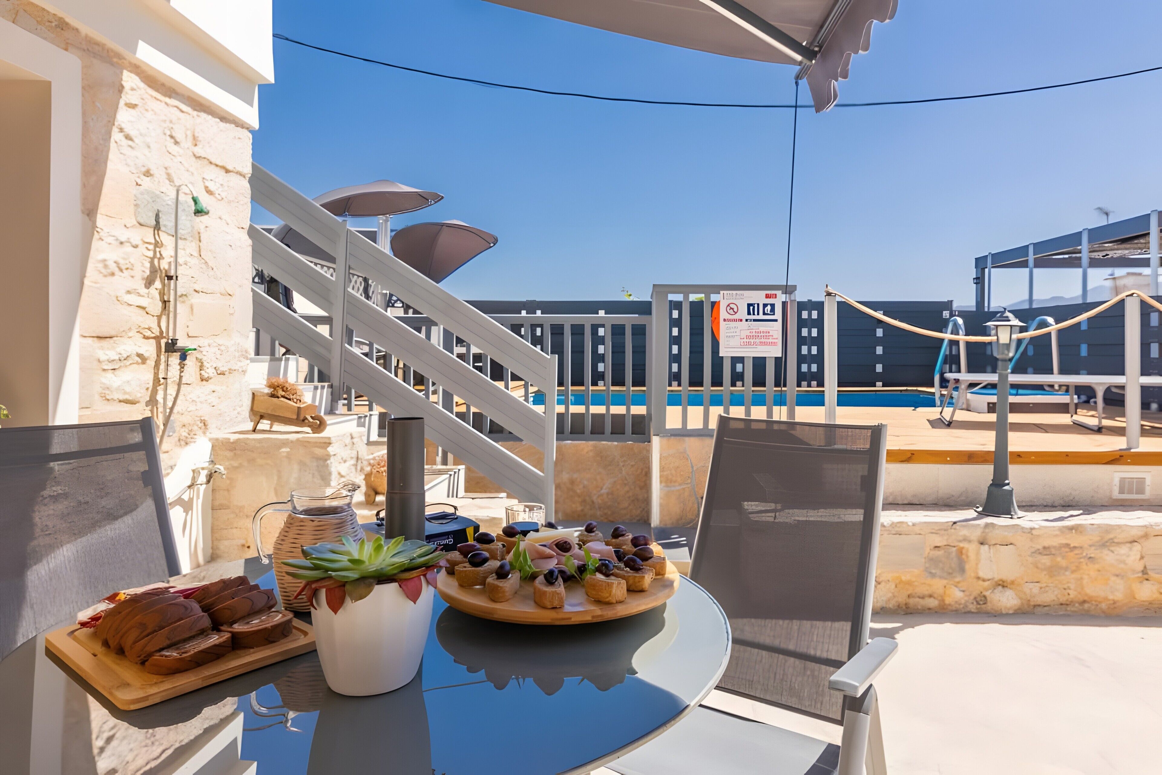 Une table avec de la nourriture, une plante en pot et une vue sur une piscine et un bâtiment.
