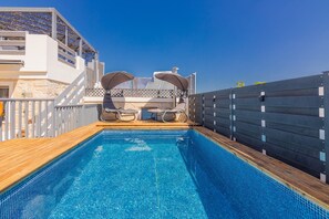 Ein Schwimmbecken mit Holzterrasse, zwei Liegestühlen und Blick auf ein Gebäude mit Balkon.